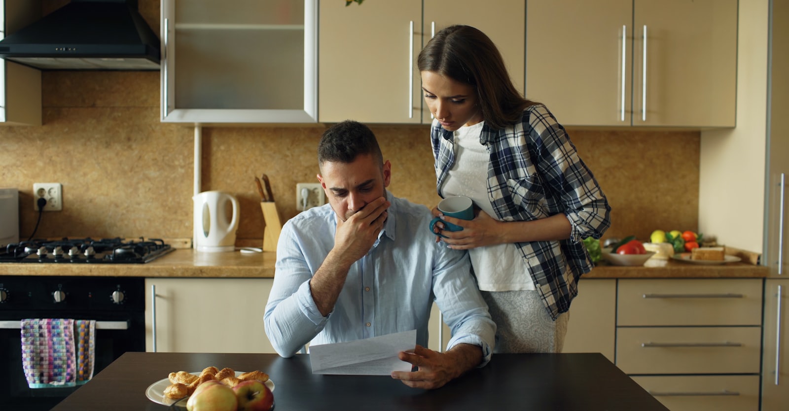 Casal na cozinha de casa lendo um documento sobre a mesa.