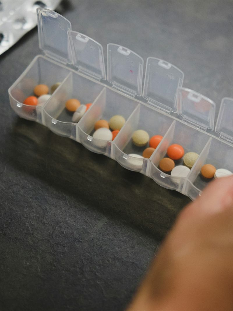 Pessoa retirando um comprimido de um organizador semanal de medicamentos.