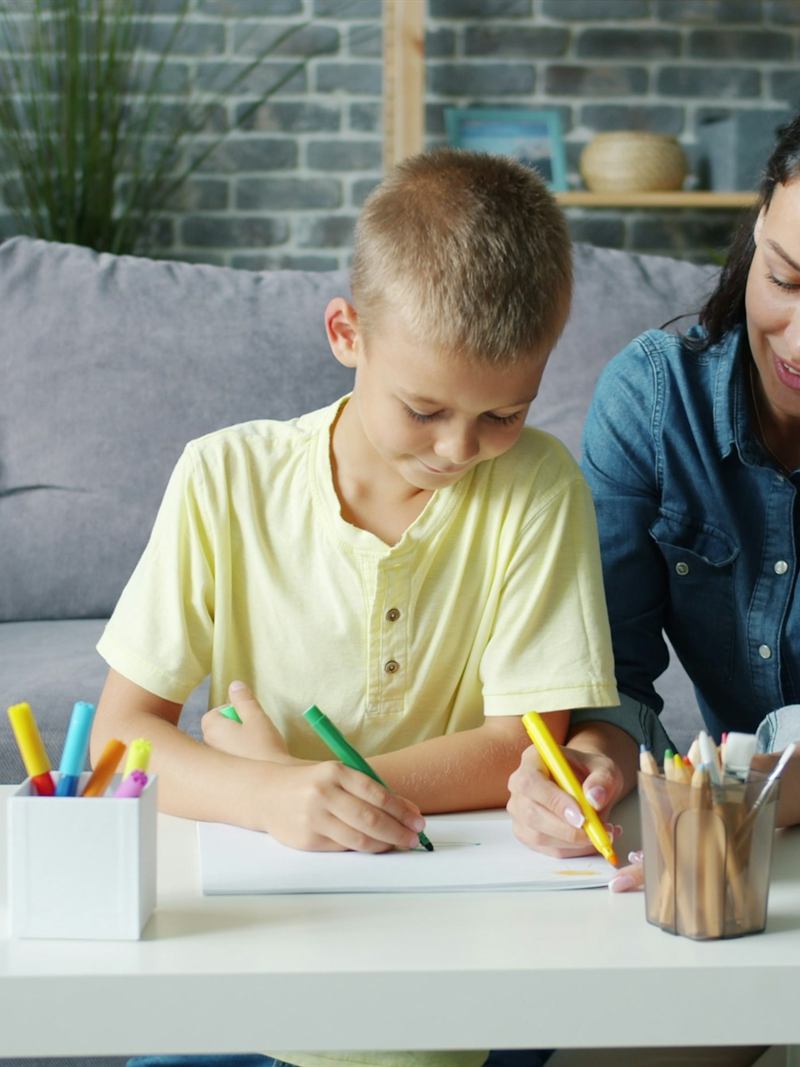 Mãe e filho desenhando juntos, à mesa.