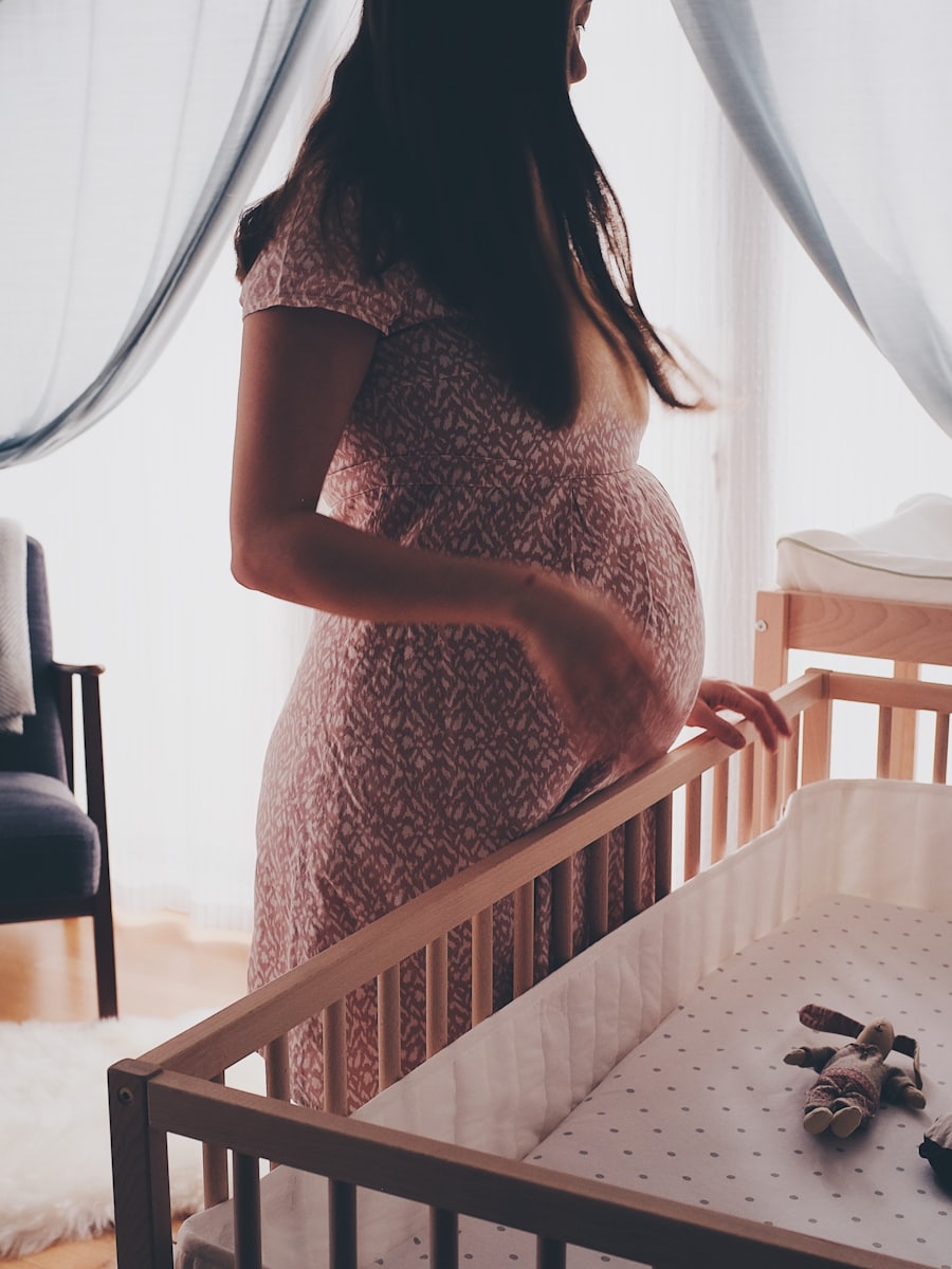 Mulher grávida em um quarto de bebê, ao lado de um berço, junto à janela.
