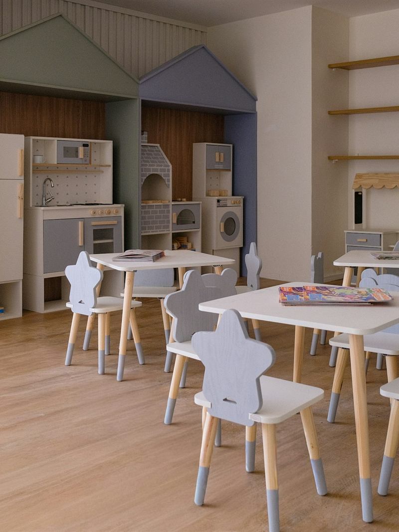 Sala de atividades infantil vazia, com mesas e cadeiras pequenas.